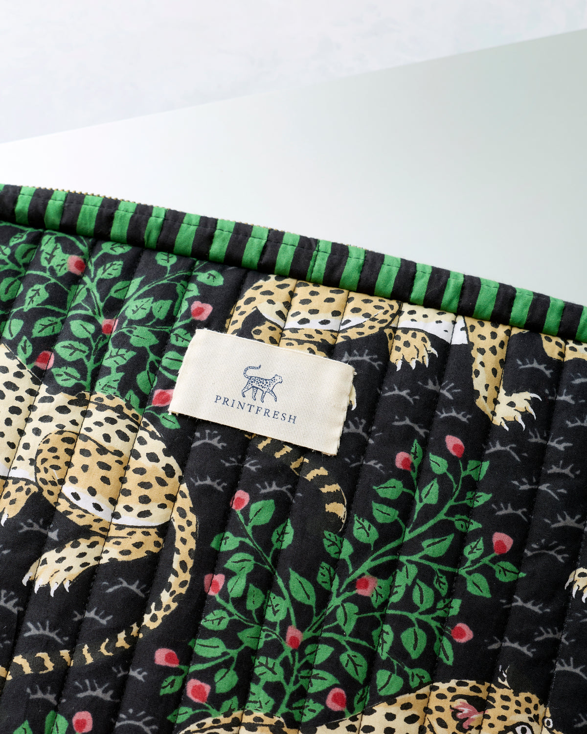 Close-up of the black quilted laptop sleeve showing green trim, leopard and leafy floral print, and Printfresh label.