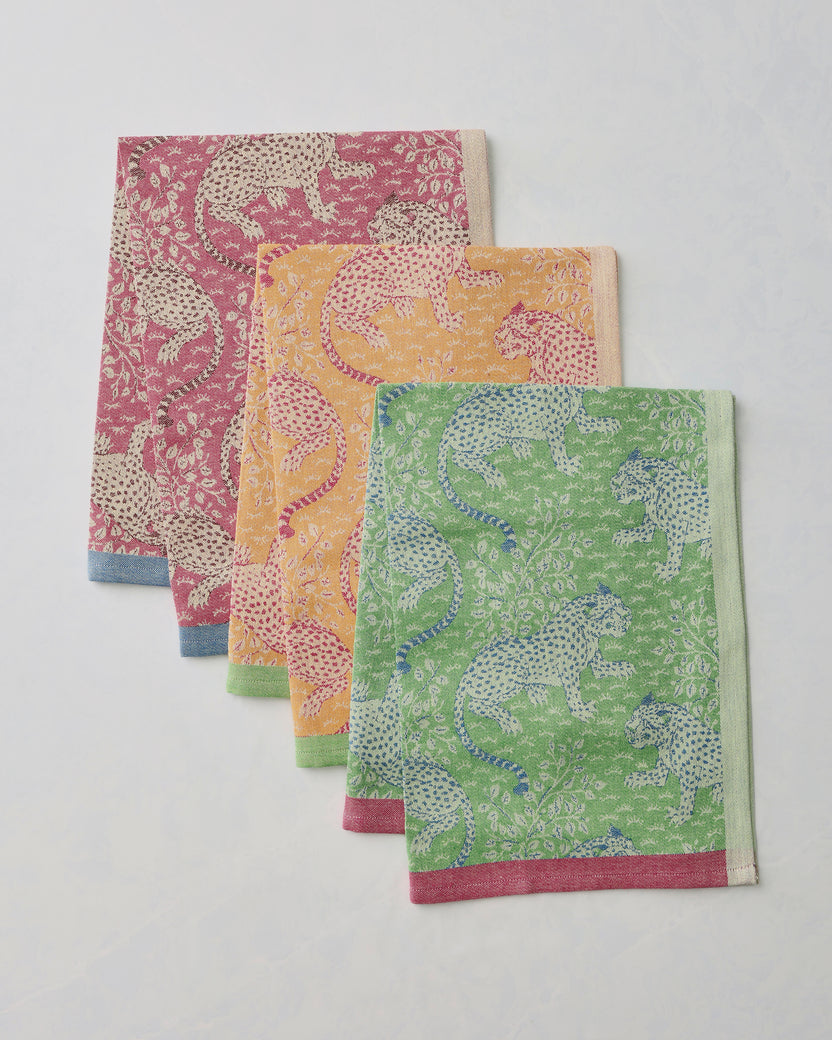 Three Bagheera jacquard tea towels in hot pink, yellow, and green, layered to show their leopard-and-floral patterns and contrasting borders.