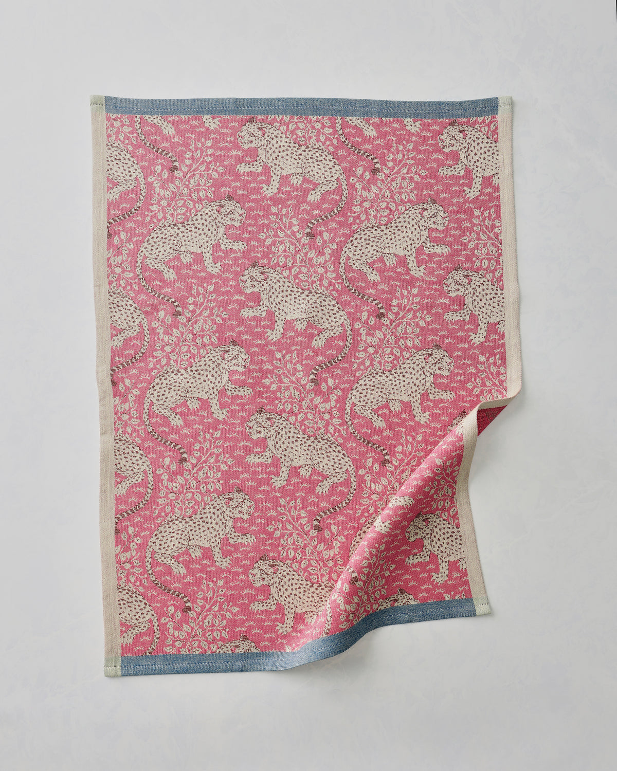 Hot pink Bagheera jacquard tea towel with a repeating leopard-and-floral pattern, shown flat with one corner folded back.