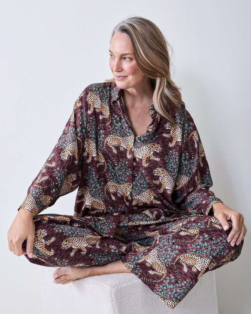 Seated view of a leopard-print satin pajama set showing the button-front shirt, cuff, and wide-leg pants.