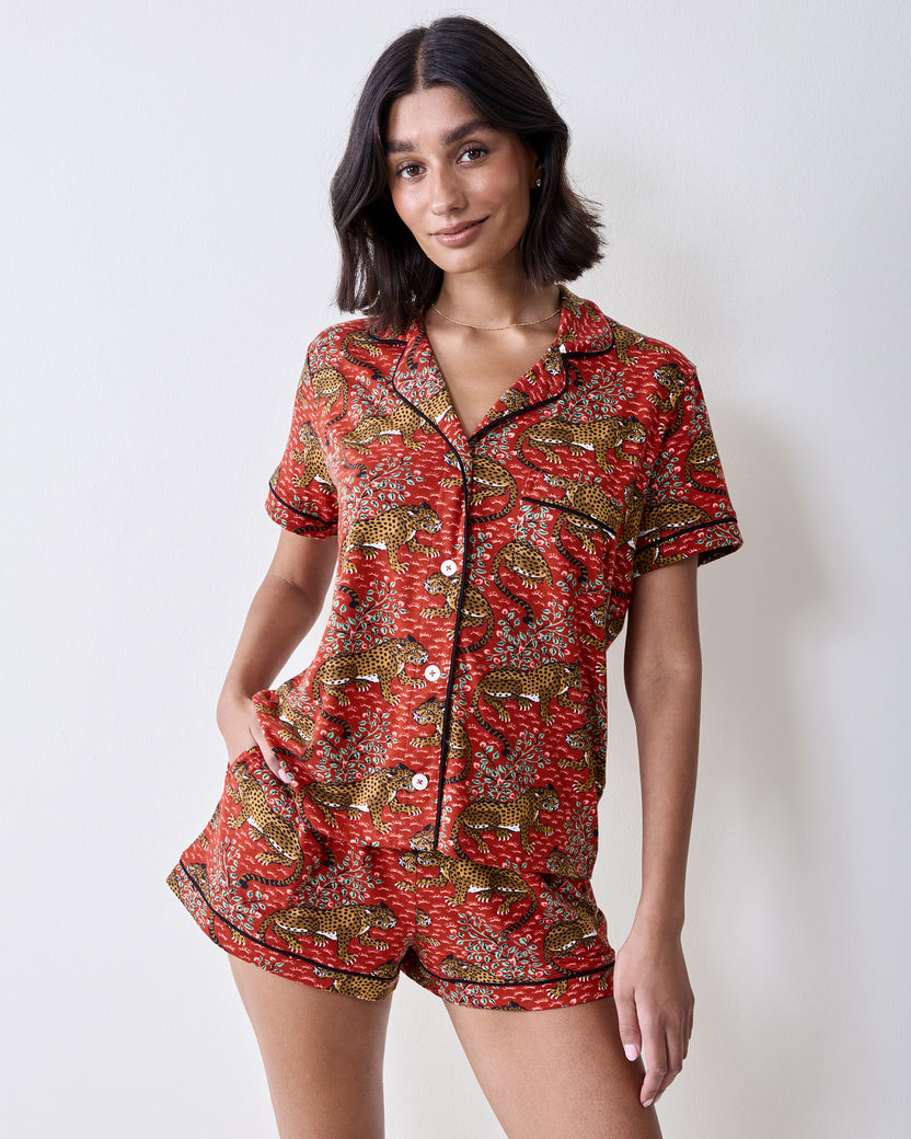 Front view of a person wearing the Scarlet Bagheera short pajama set with a short-sleeved button-front top and matching shorts in a leopard and botanical print.