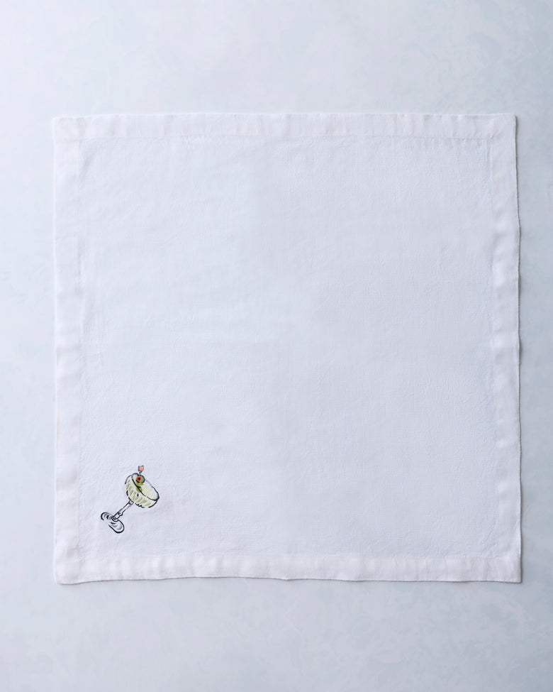 White square dinner napkin embroidered with a small cocktail glass and garnish motif near one corner.