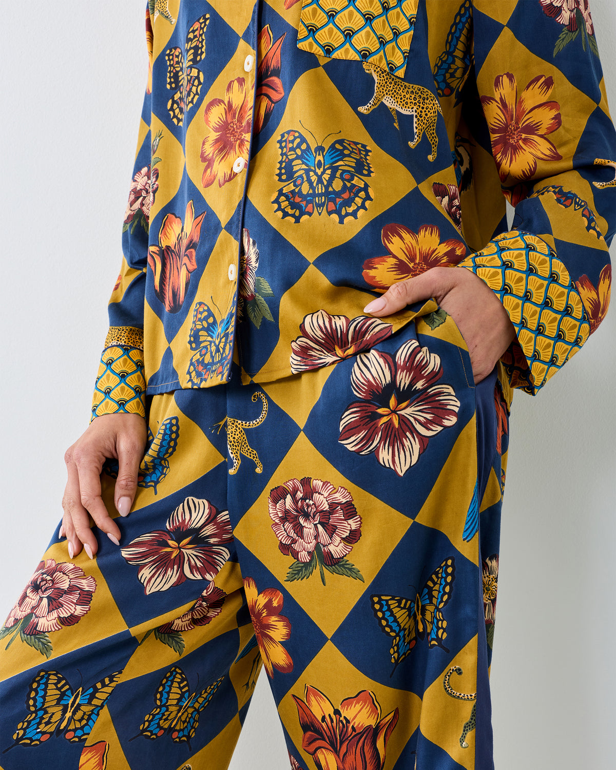 Close-up of the Botanical Checkerboard Rittenhouse pajama set showing the long-sleeve button-front top, pocket, and matching pants with floral, butterfly, and leopard motifs.