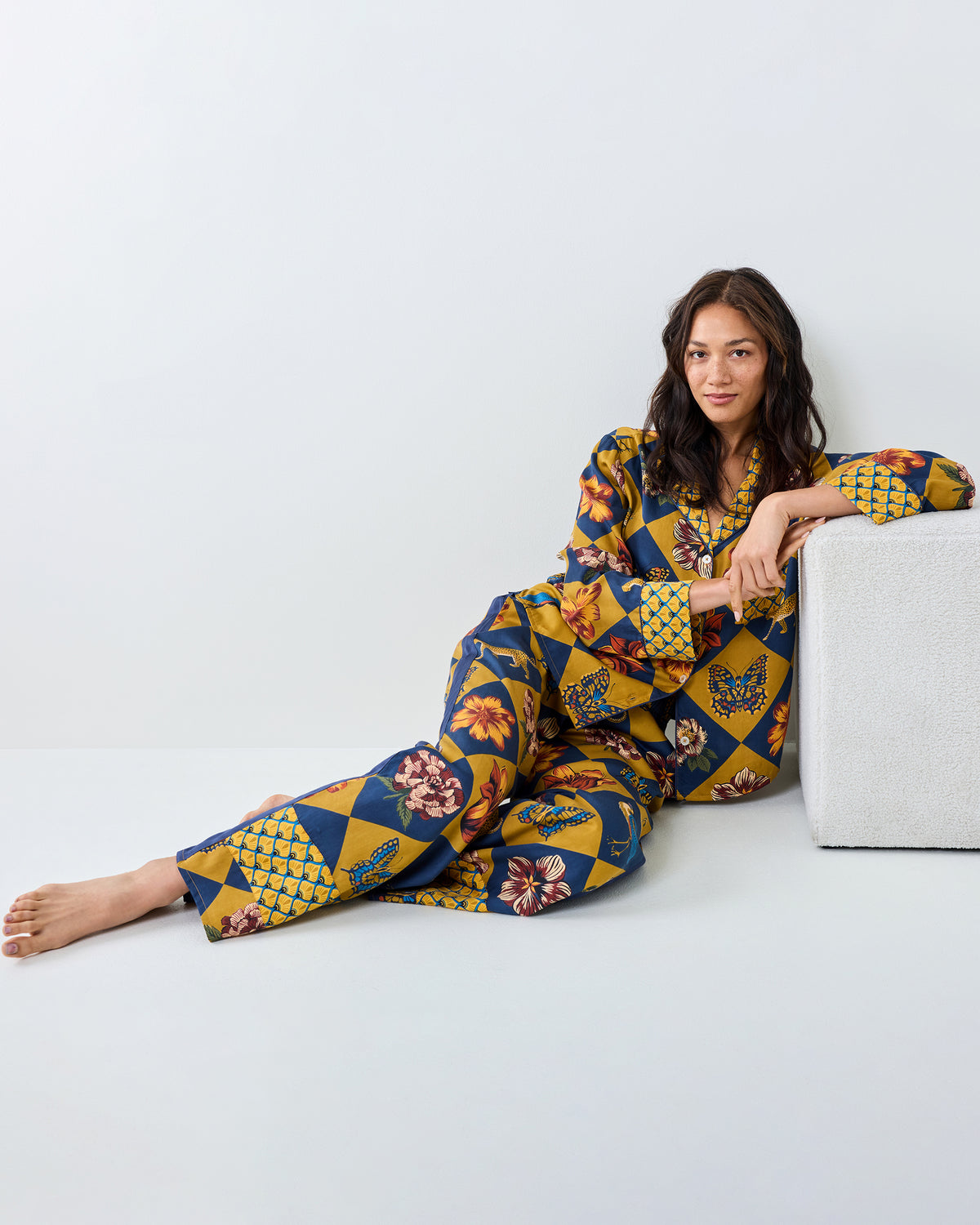 Person reclining beside a low table while wearing the Golden Hour Botanical Checkerboard long-sleeved top and matching wide-leg pants.