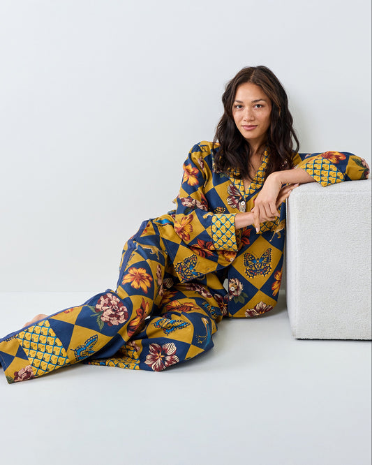 Person reclining beside a low table while wearing the Golden Hour Botanical Checkerboard long-sleeved top and matching wide-leg pants.