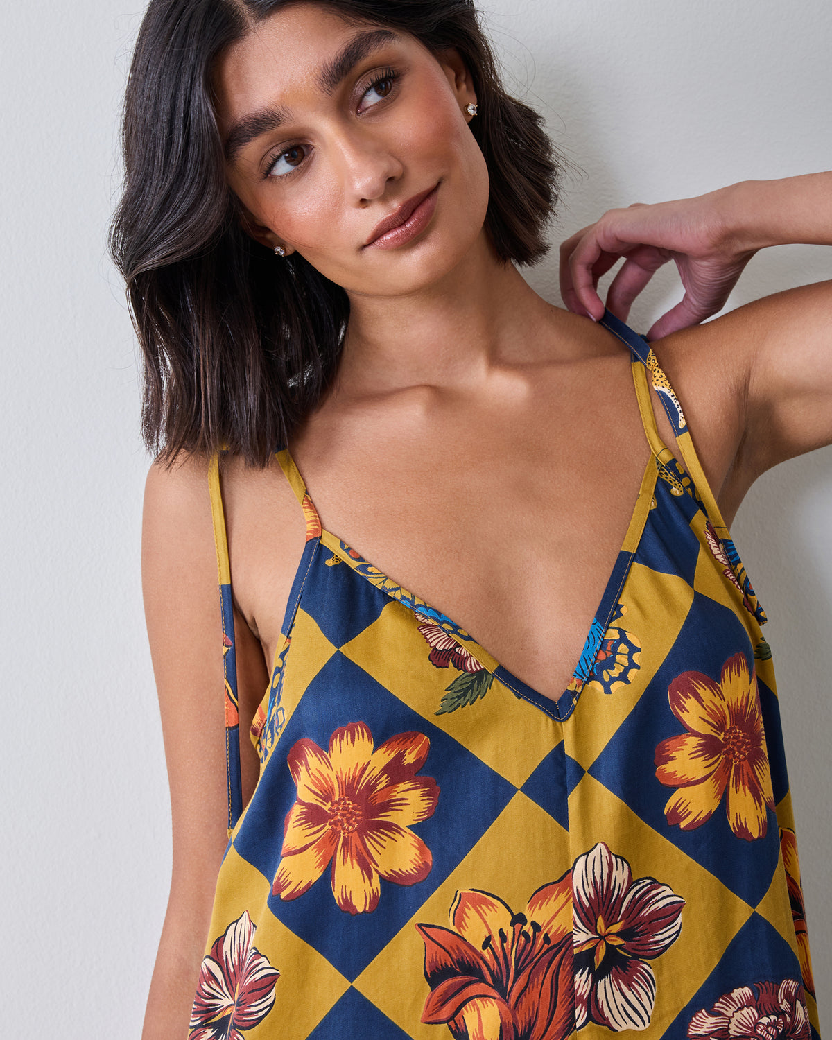 Close view of a person wearing a navy and golden checkerboard jumpsuit with floral print, V-neckline, and adjustable straps.