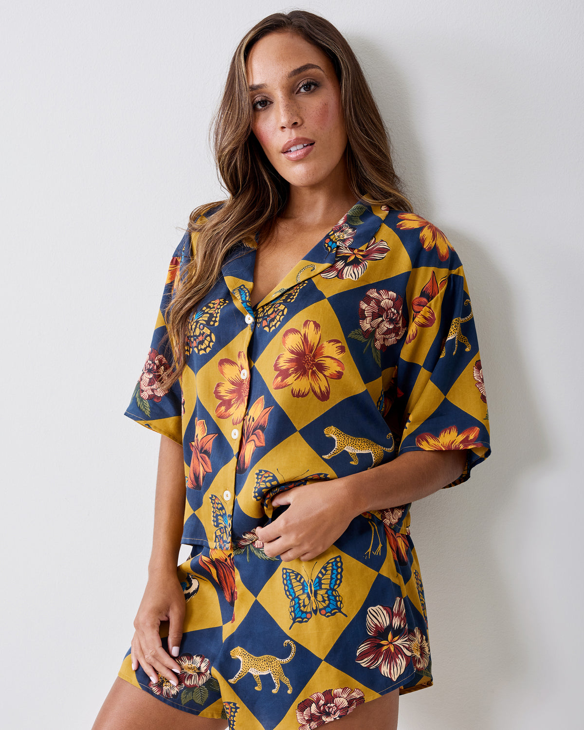 Front view of the Botanical Checkerboard Sweet Dreams pajama set with a short-sleeve button-front top and matching shorts featuring floral, butterfly, and leopard motifs.