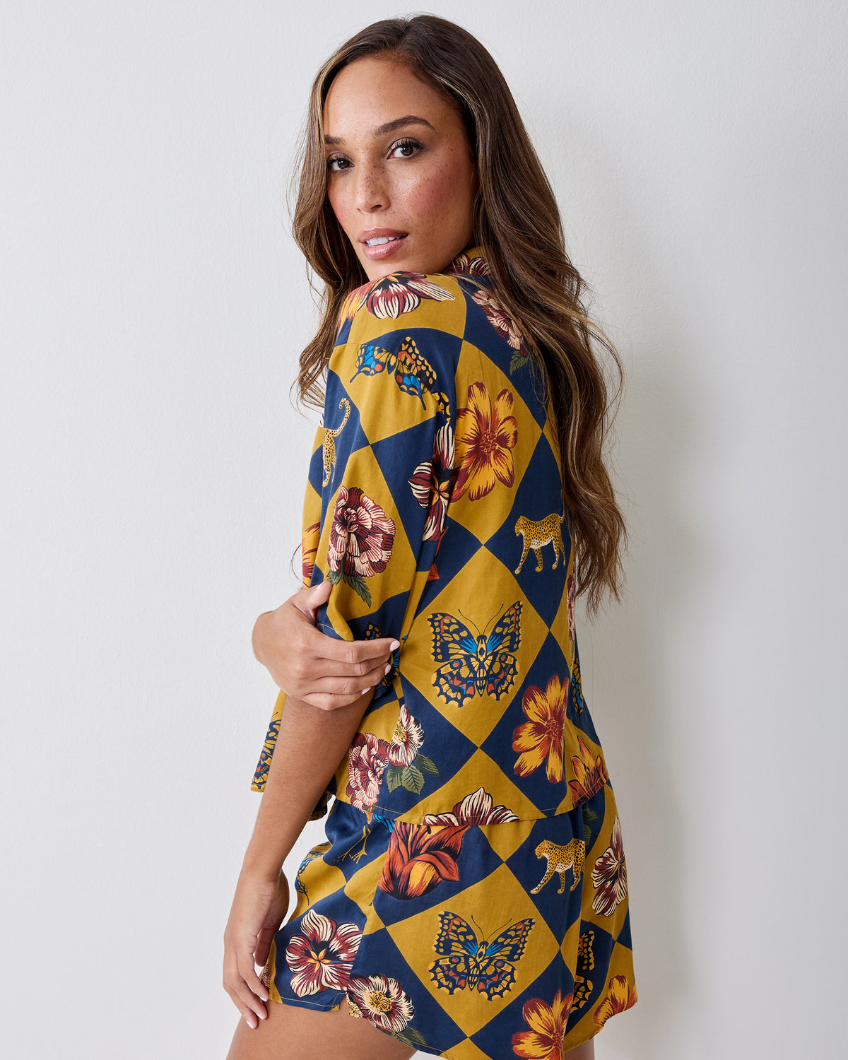 Side and back view of a short pajama set with a navy-and-gold checkerboard print featuring flowers, butterflies, and leopards.