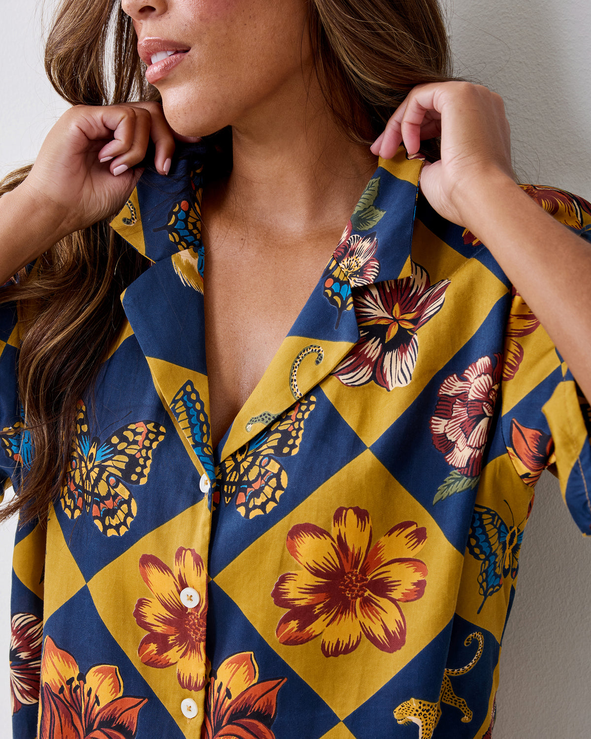 Close-up of the Botanical Checkerboard Sweet Dreams pajama top showing the notched collar, white buttons, and floral, butterfly, and leopard print.