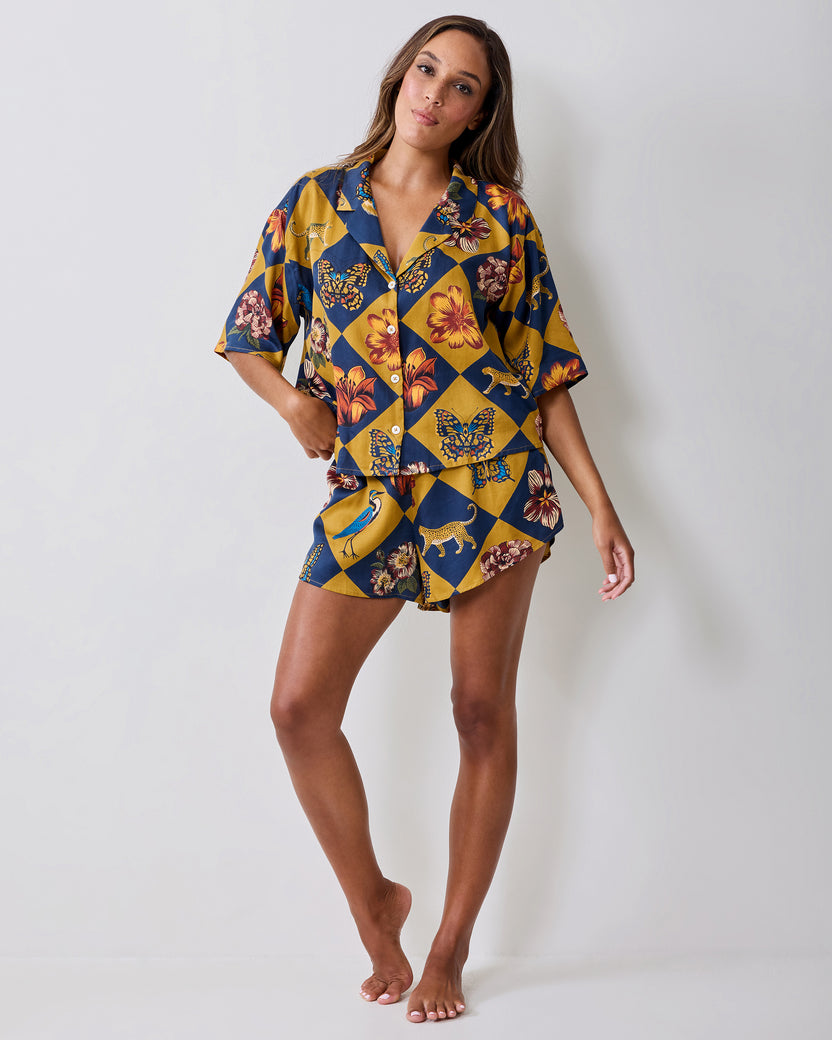 Full-length front view of the Botanical Checkerboard pajama top and shorts on a model, with a navy and golden checkerboard print featuring botanical and animal motifs.