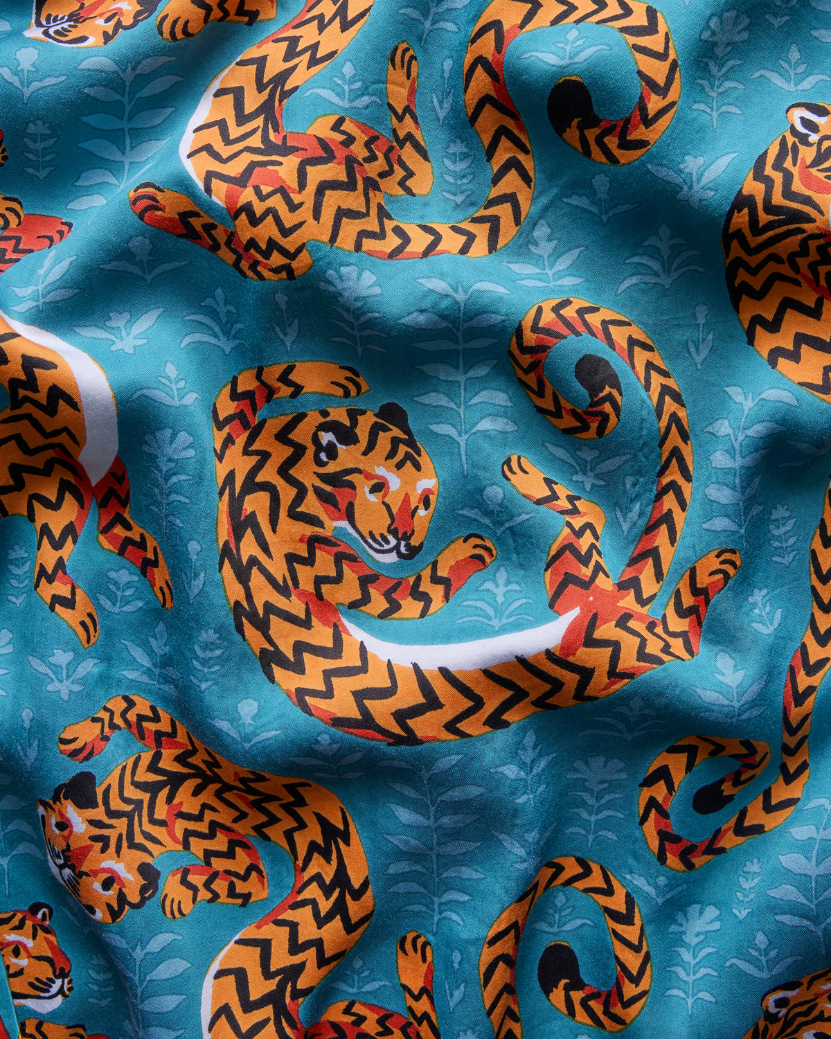 Close-up of turquoise Twisted Tiger print fabric with orange-and-black curled tigers and pale botanical motifs.
