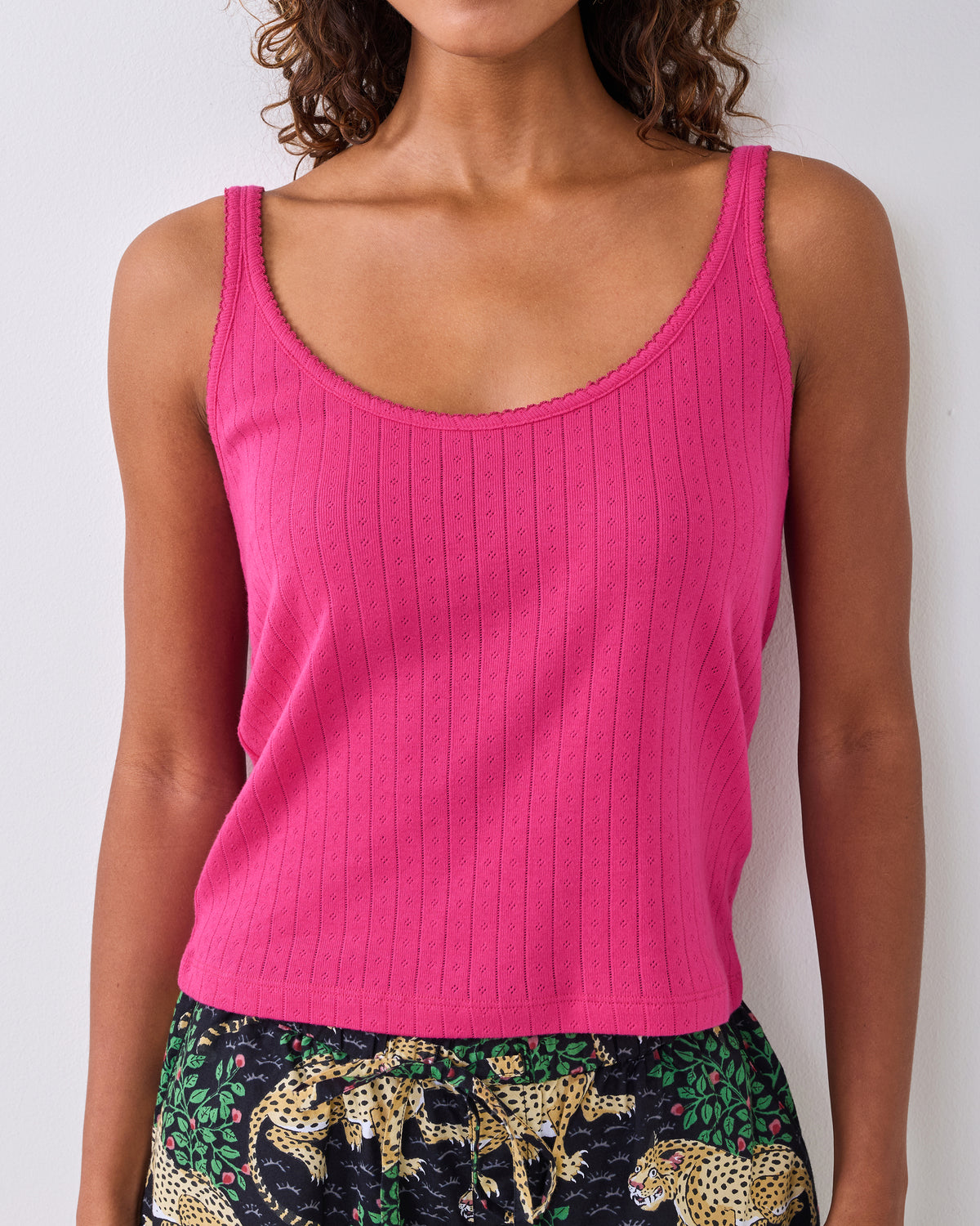 Bright pink sleeveless pointelle tank top with lace-trimmed neckline and shoulder straps, shown on a person.