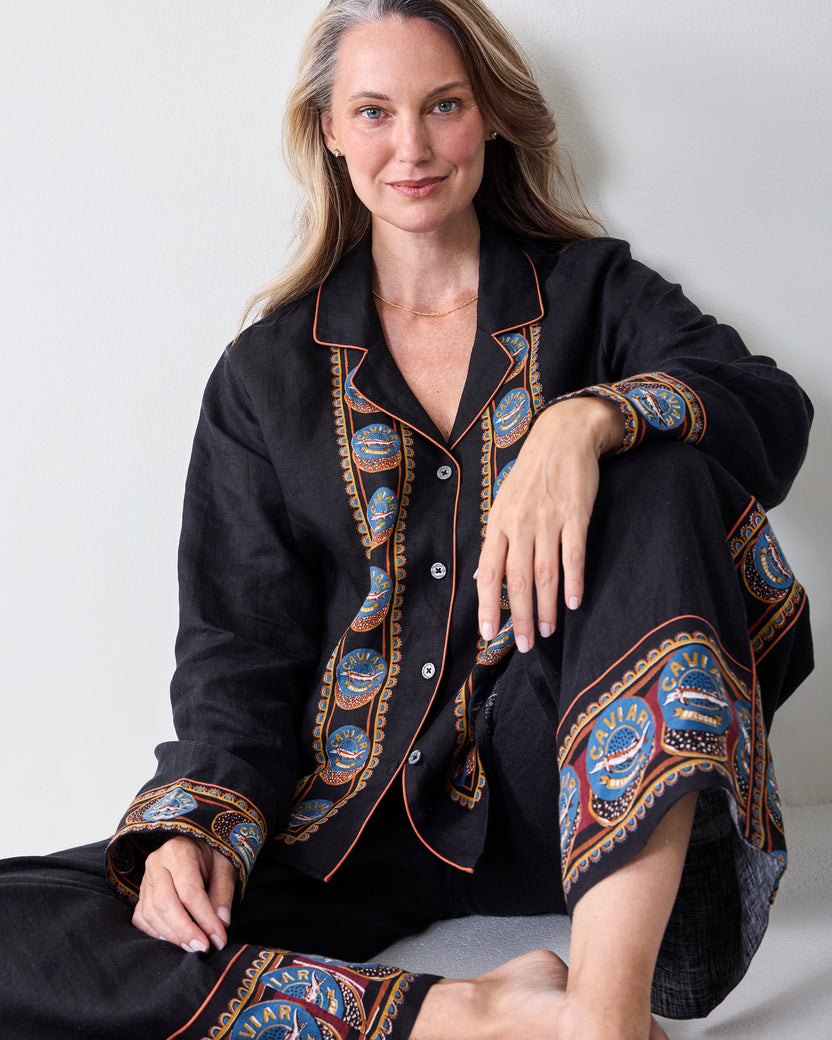 Seated view of the black tunic and wide-leg pants with decorative patterned trim on the front, cuffs, and pant legs.