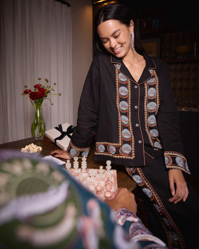 Person wearing the black Addison pajama shirt and pants with blue-and-orange circular trim, leaning over a chessboard.