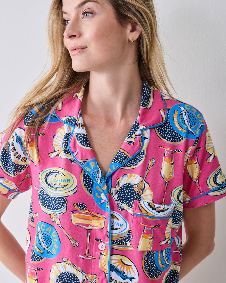 Front view of the hot pink Champagne & Caviar short pajama shirt with a notched collar, chest pocket, buttons, and printed caviar-themed pattern.