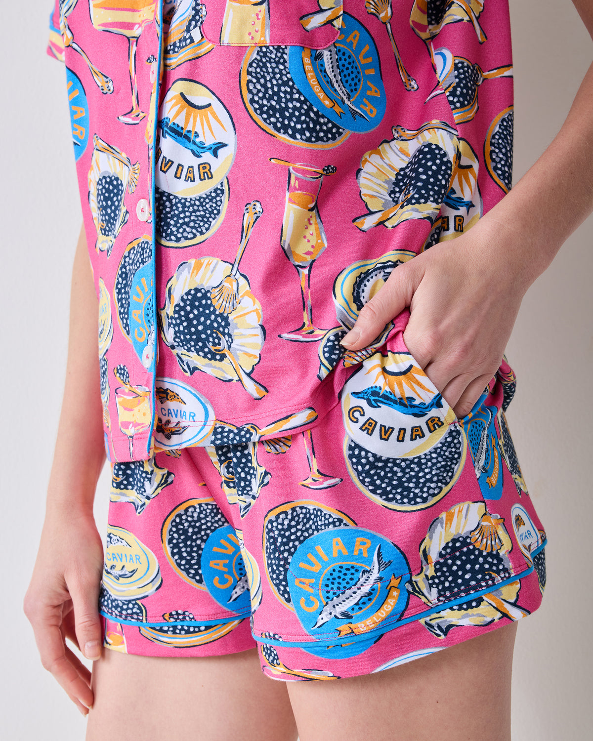 Close-up of the hot pink Champagne & Caviar short pajama set, showing the patterned shirt and shorts with caviar tins, glasses, and spoons.