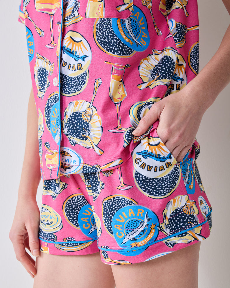 Close-up of the hot pink Champagne & Caviar short pajama set, showing the patterned shirt and shorts with caviar tins, glasses, and spoons.