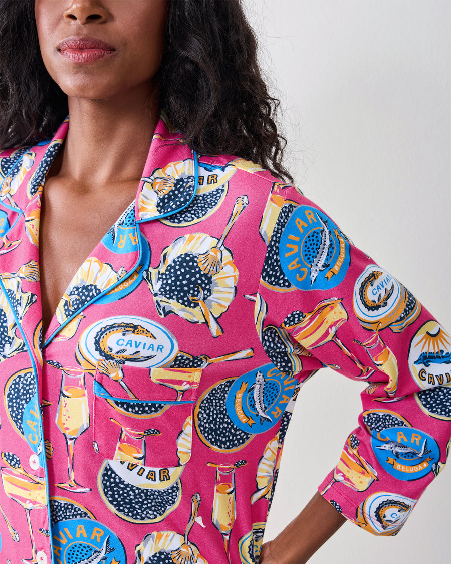 Close-up of the hot pink Champagne & Caviar sleep shirt showing its notched collar, contrasting trim, long sleeves, and caviar-themed print.
