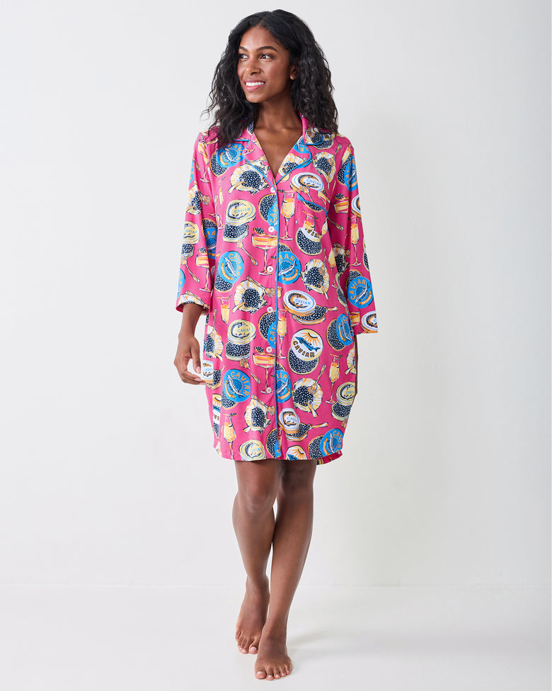 Full-length front view of a person wearing the hot pink Champagne & Caviar sleep shirt with long sleeves and a caviar-themed print.