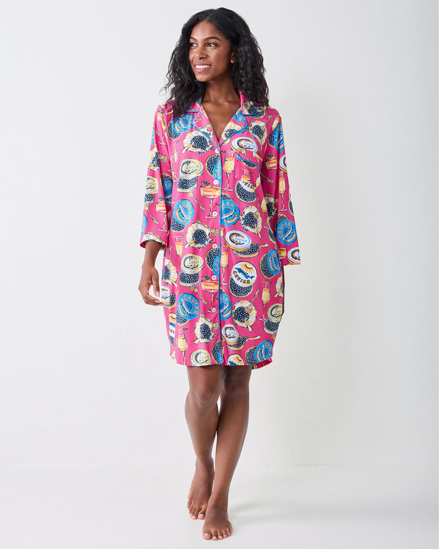 Full-length front view of a person wearing the hot pink Champagne & Caviar sleep shirt with long sleeves and a caviar-themed print.