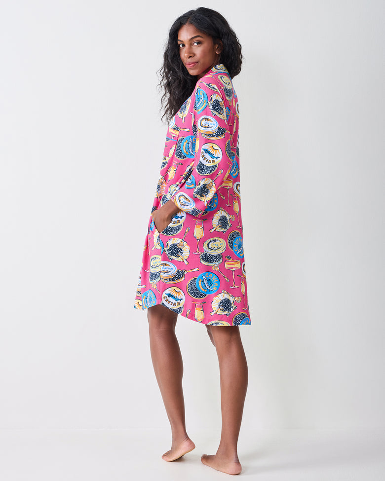 Back and side view of a person wearing the hot pink Champagne & Caviar sleep shirt, showing the shirt-length hem, long sleeves, and printed pattern.