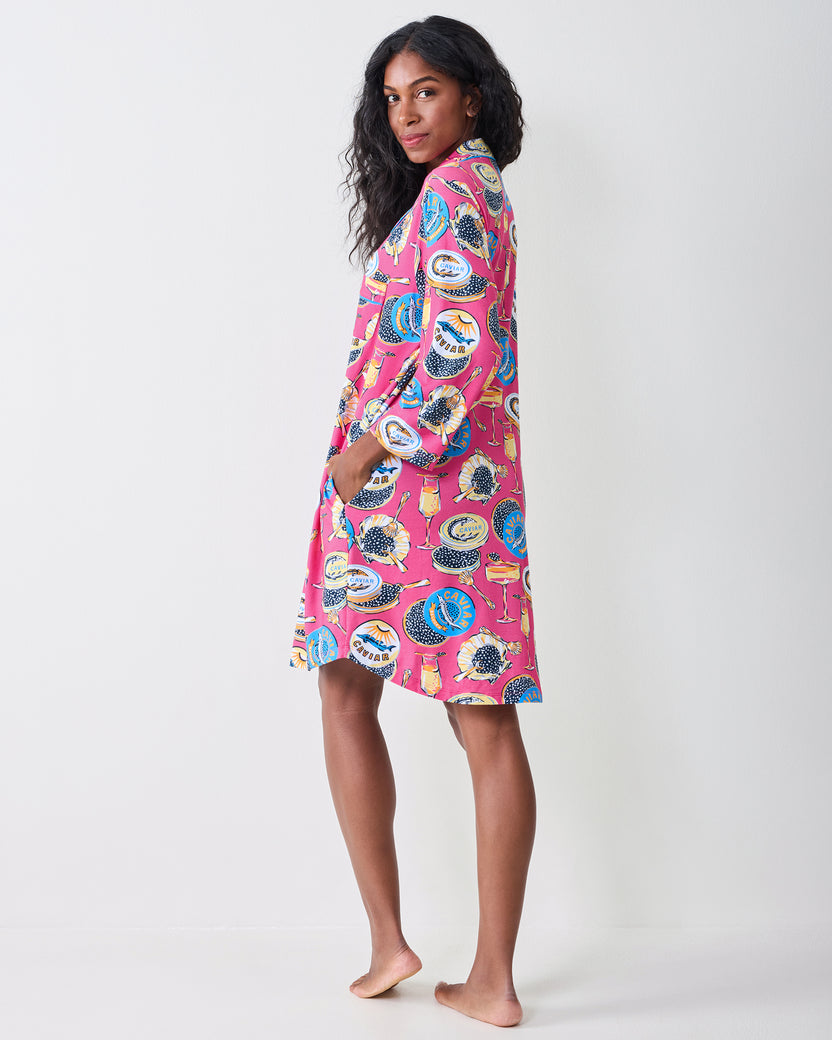 Back and side view of a person wearing the hot pink Champagne & Caviar sleep shirt, showing the shirt-length hem, long sleeves, and printed pattern.