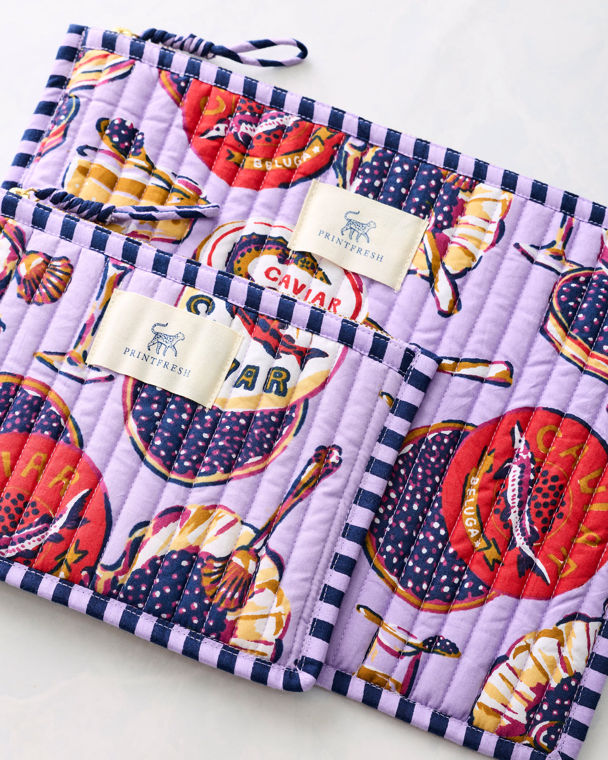 Lavender Champagne and Caviar flat pouch duo with illustrated champagne and caviar-themed print, zippers, and Printfresh labels.