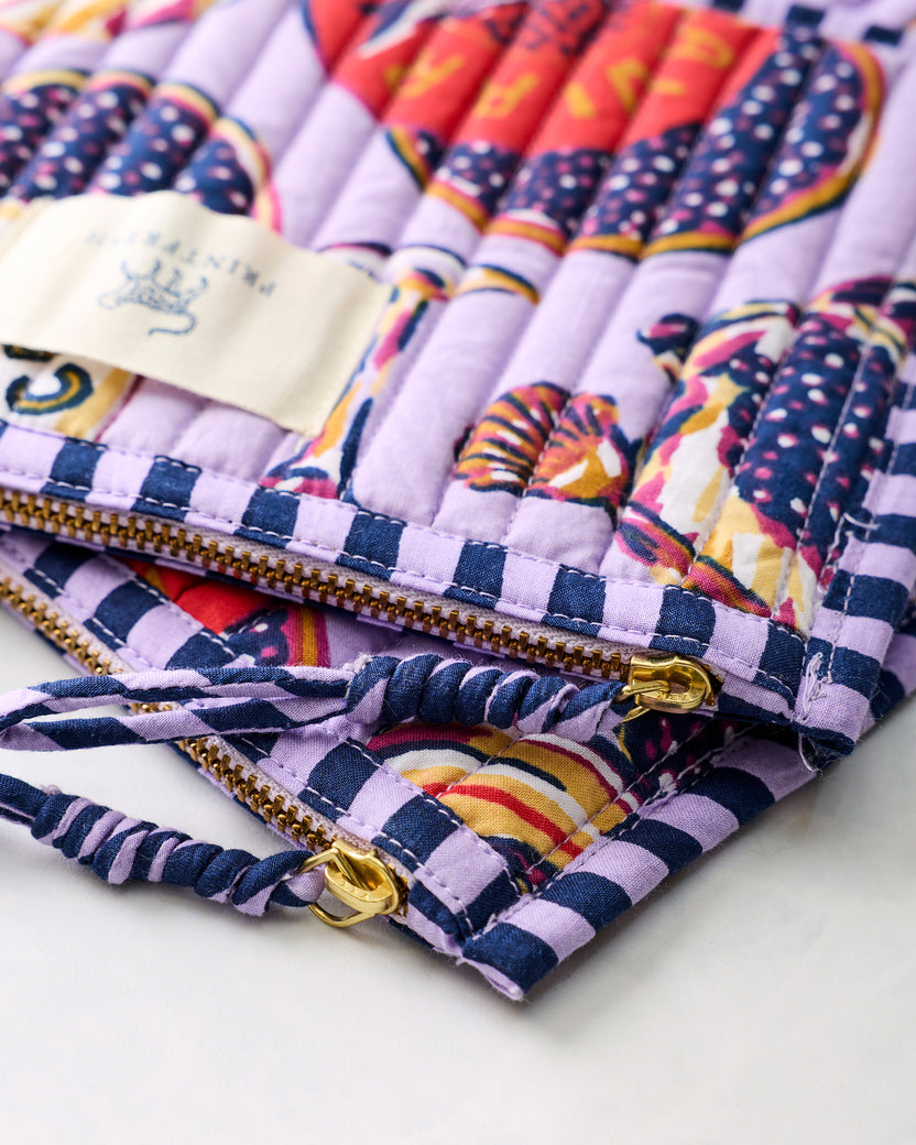 Close-up of the lavender Champagne and Caviar pouch duo showing gold-toned zippers, pulls, and twisted fabric wrist loops.