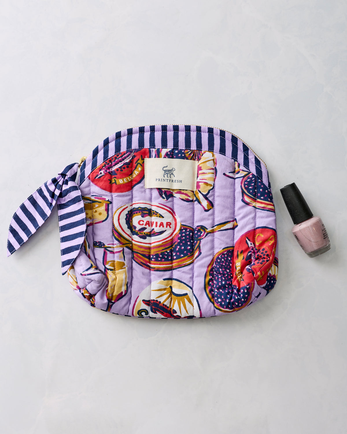 Lavender Champagne & Caviar makeup bag shown beside a bottle of nail polish.
