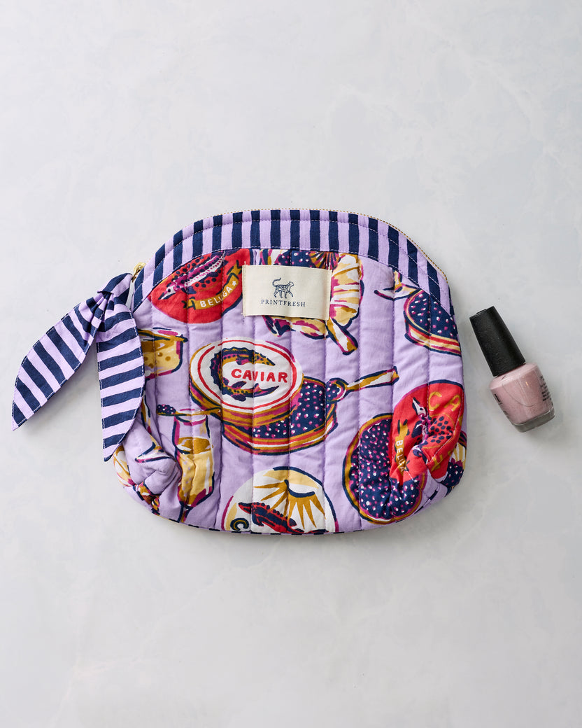 Lavender Champagne & Caviar makeup bag shown beside a bottle of nail polish.