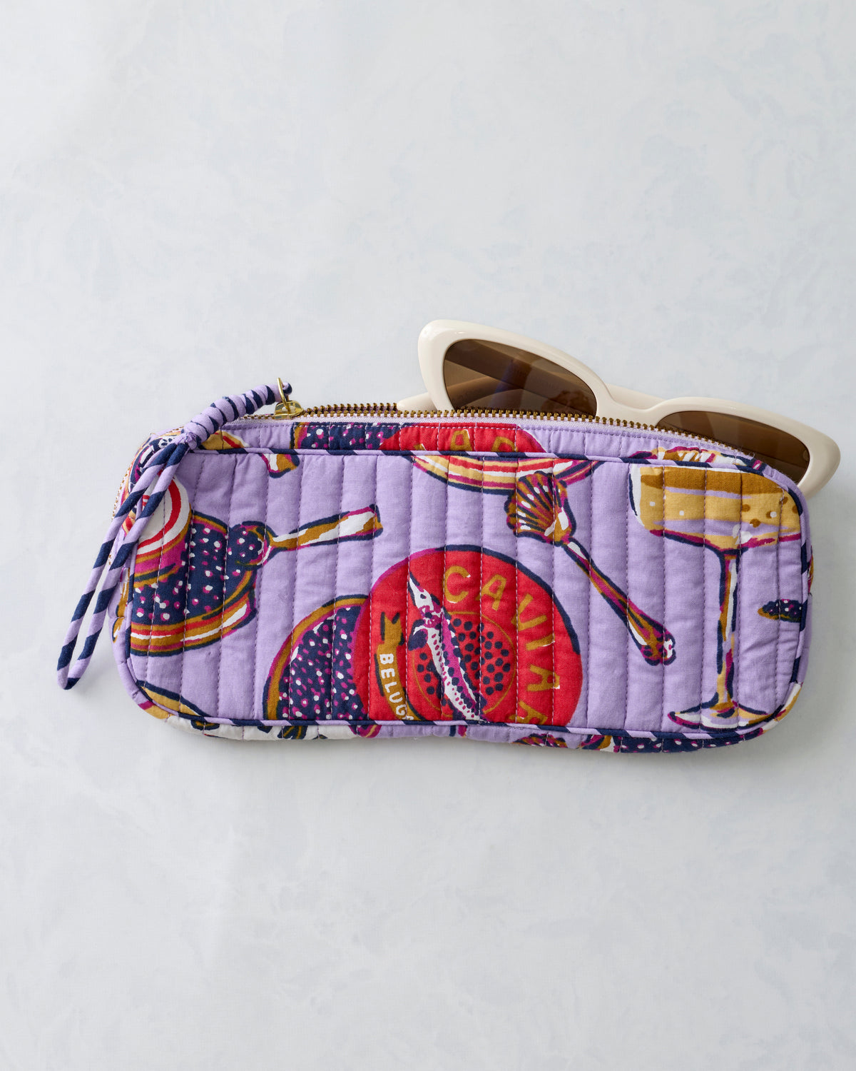 Lavender quilted zippered sunglasses case shown open with white-framed sunglasses partly inside.
