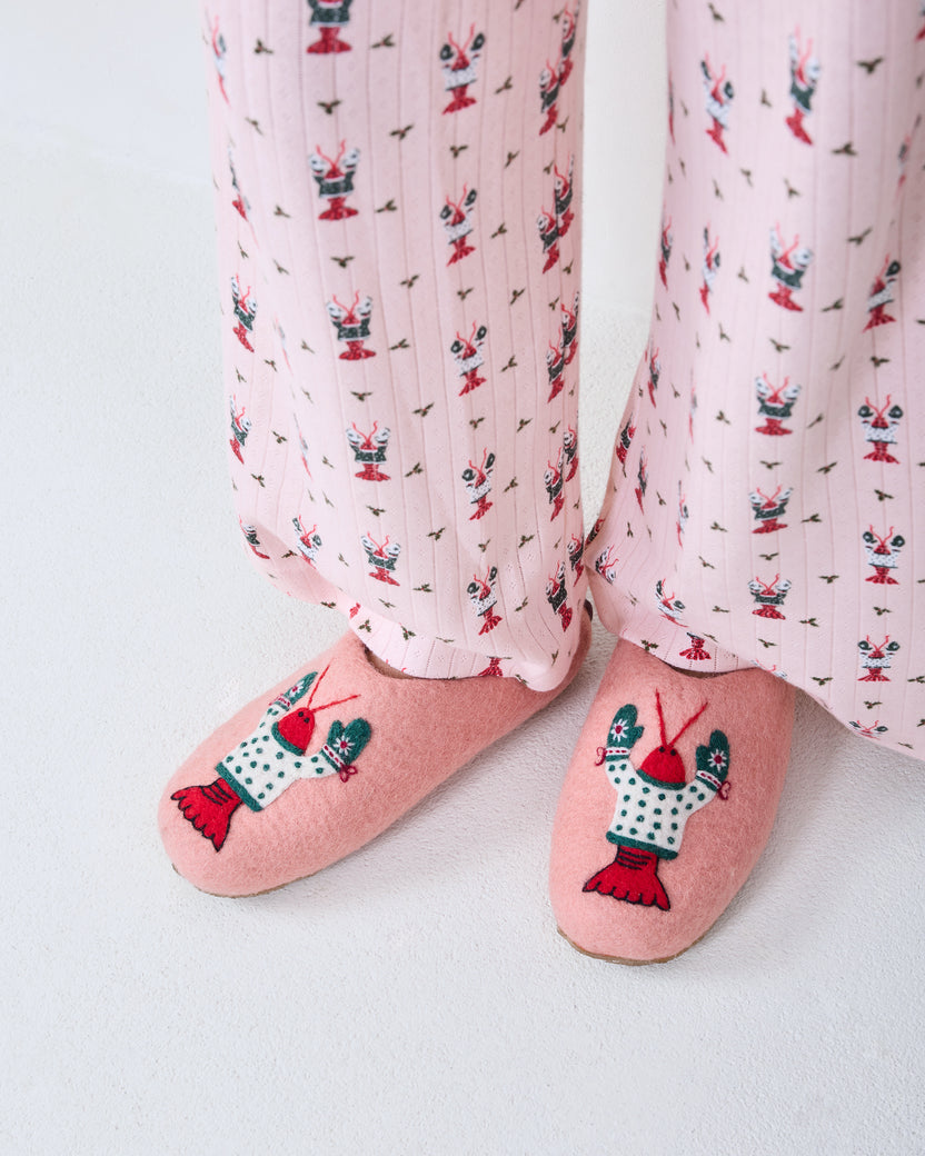 Close-up of Christmas Claws pajama pants worn with pink slippers featuring embroidered claw motifs.