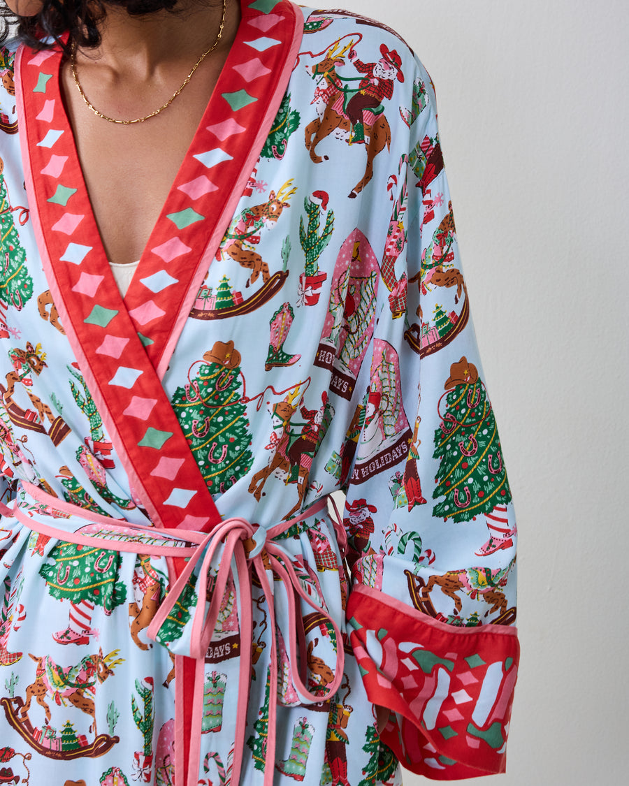 Close-up of the pale blue Cowboy Christmas robe showing the printed holiday motifs, red patterned trim, tie belt, and cuff.