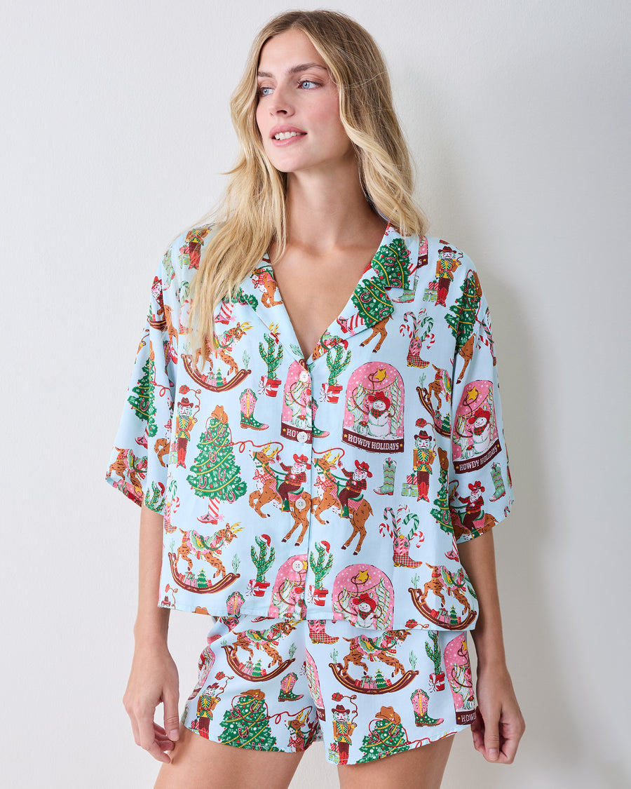 Front view of a short-sleeved button-down pajama top and matching shorts with a Christmas cowboy print.