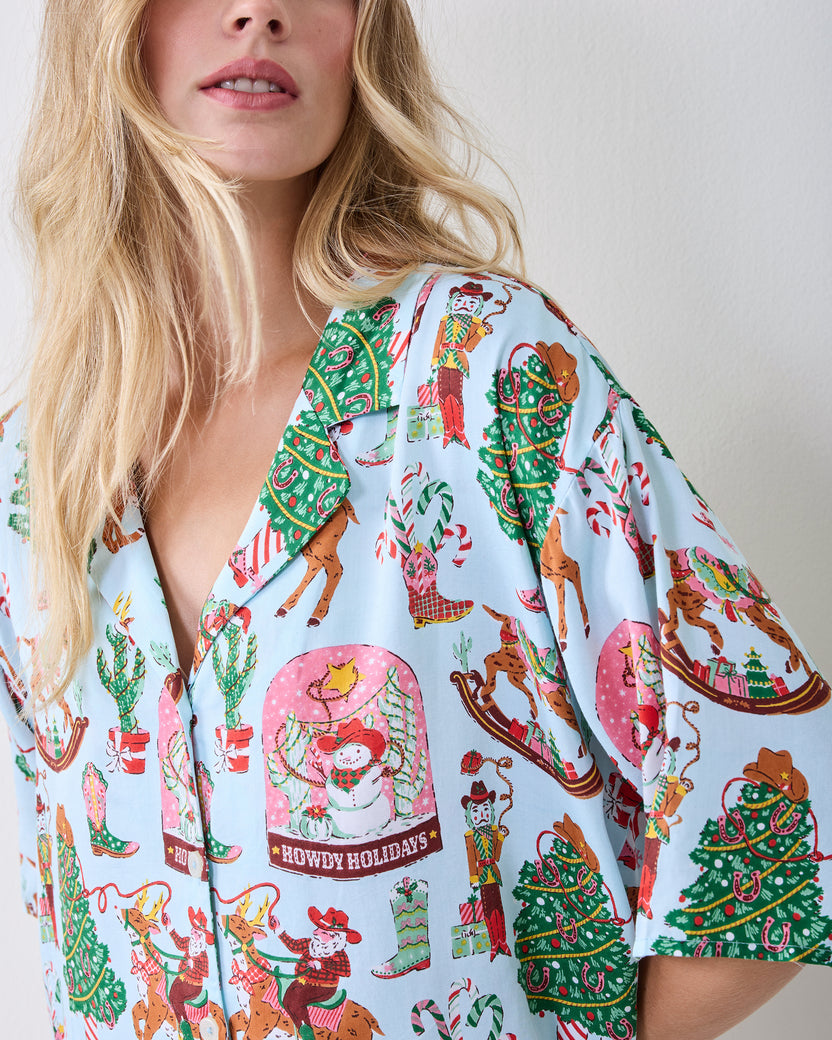 Close-up of the short-sleeve button-down top in the Cowboy Christmas print, showing reindeer, Christmas trees, boots, and snow globes.