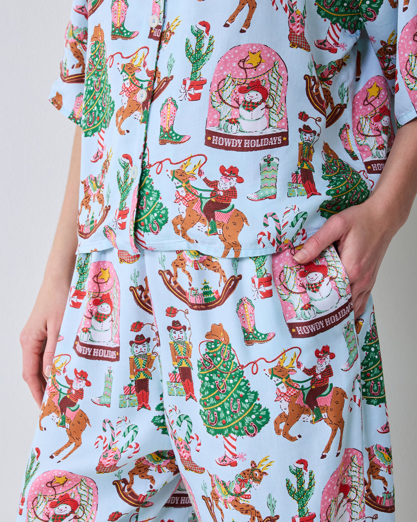 Close-up of the Cowboy Christmas print on the button-down top and wide-leg pants, with a hand in the pants pocket.