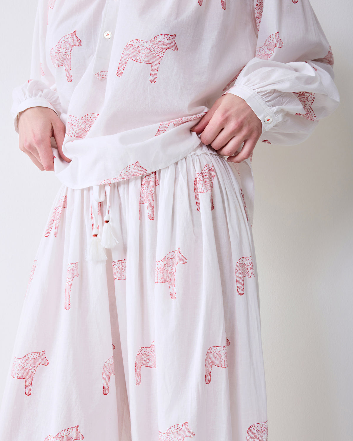 Close-up of the Arctic Rose Dala Horse Millie Set showing the white long-sleeve top and gathered pants with pink horse prints, ribbon tie, and lace hem.