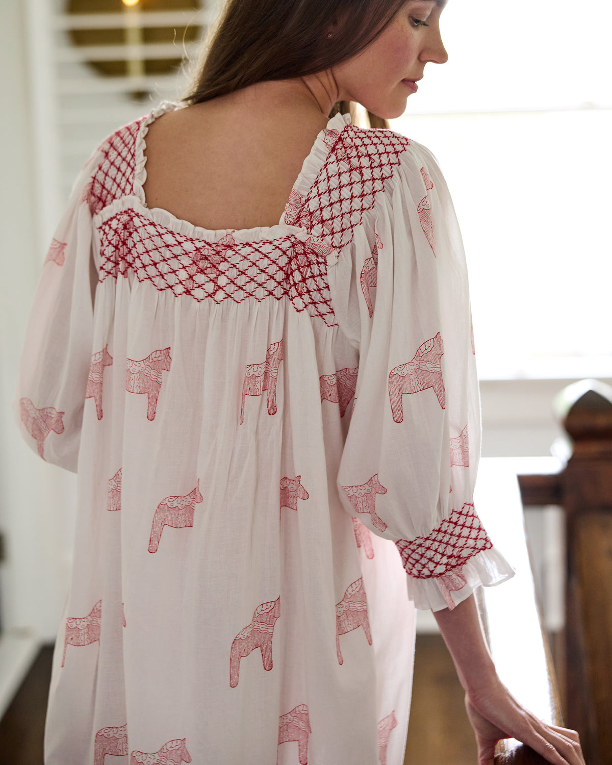 Close-up back view of a white nightgown showing the red smocked neckline and cuff trim with pink horse prints.