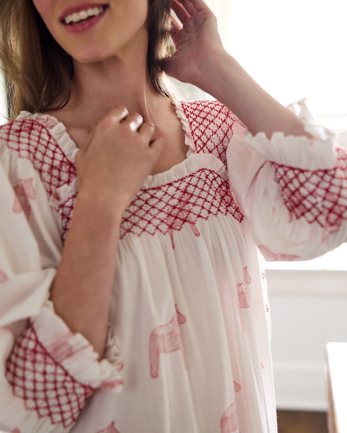 Close-up front view of a white nightgown showing the red smocked neckline and cuff trim with pink horse prints.