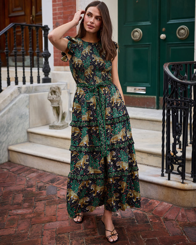 Front view of the Bagheera Ready To Ruffle Maxi dress in Ink, showing ruffled sleeves, waist tie, leopard and leafy-branch print, and tiered skirt outdoors.