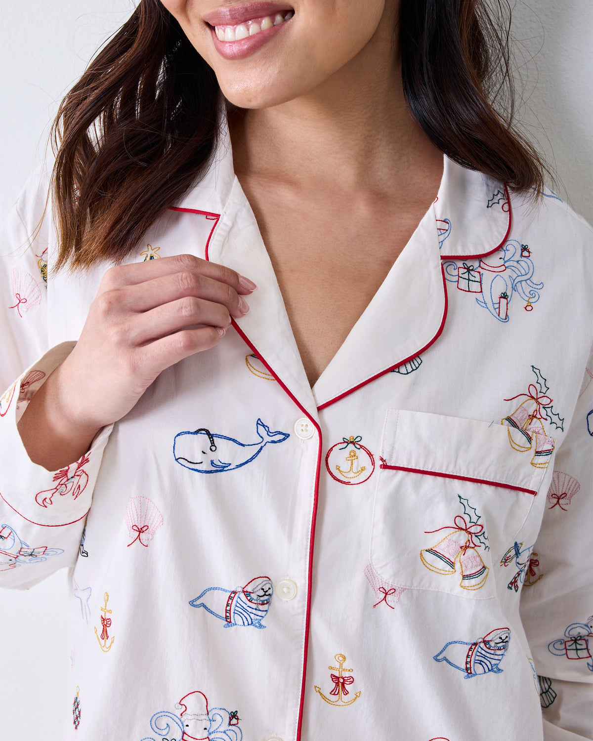 Close-up of the Cloud long pajama shirt showing red piping, buttons, chest pocket, and embroidered whale, seal, bell, anchor, and other motifs.