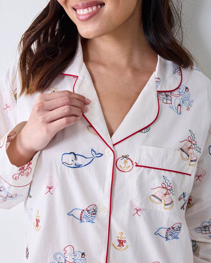 Close-up of the Cloud long pajama shirt showing red piping, buttons, chest pocket, and embroidered whale, seal, bell, anchor, and other motifs.