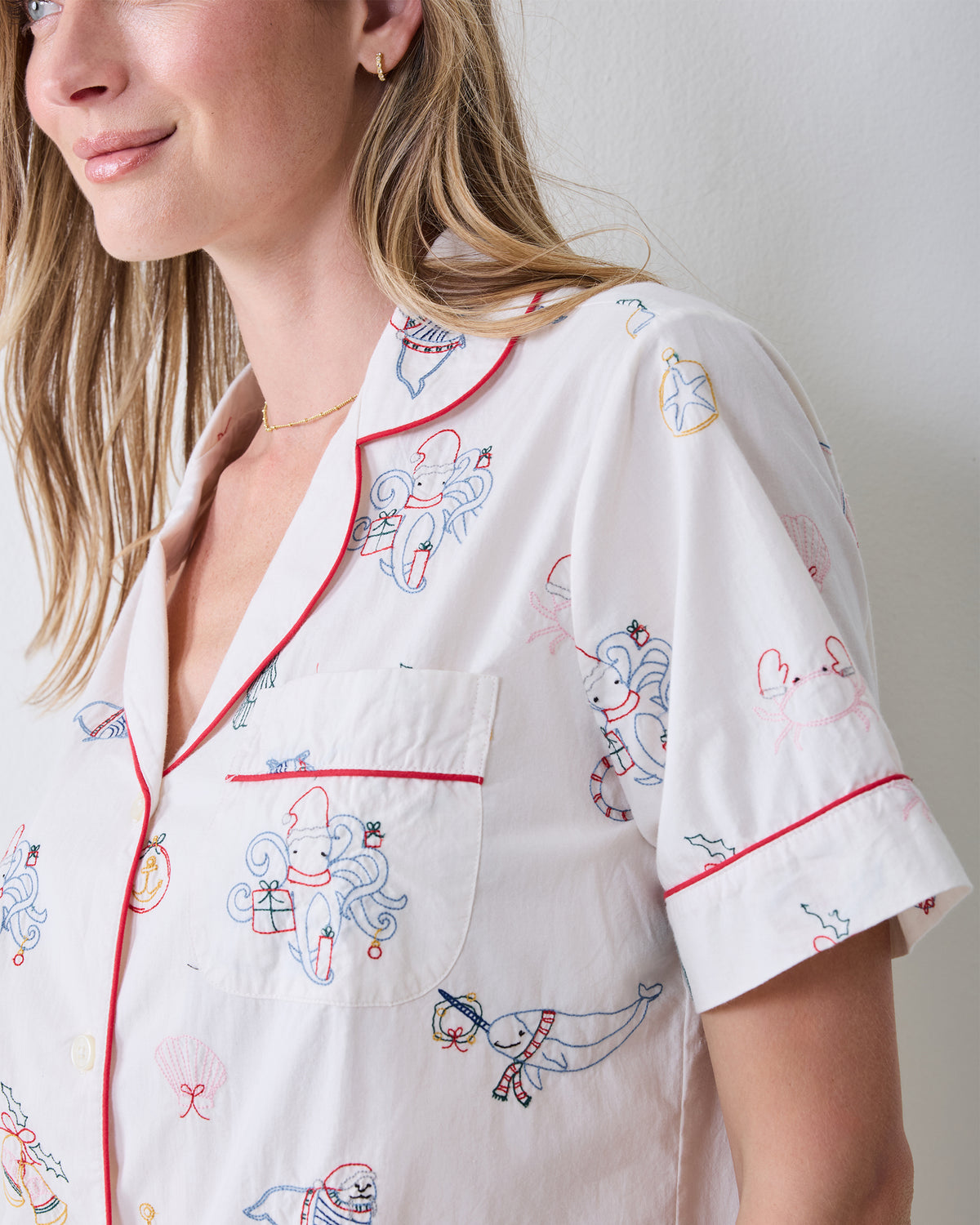 Close-up of the embroidered Yule Tides cloud Short PJ Set showing the collar, chest pocket, red piping, sleeve cuff, and stitched motifs.