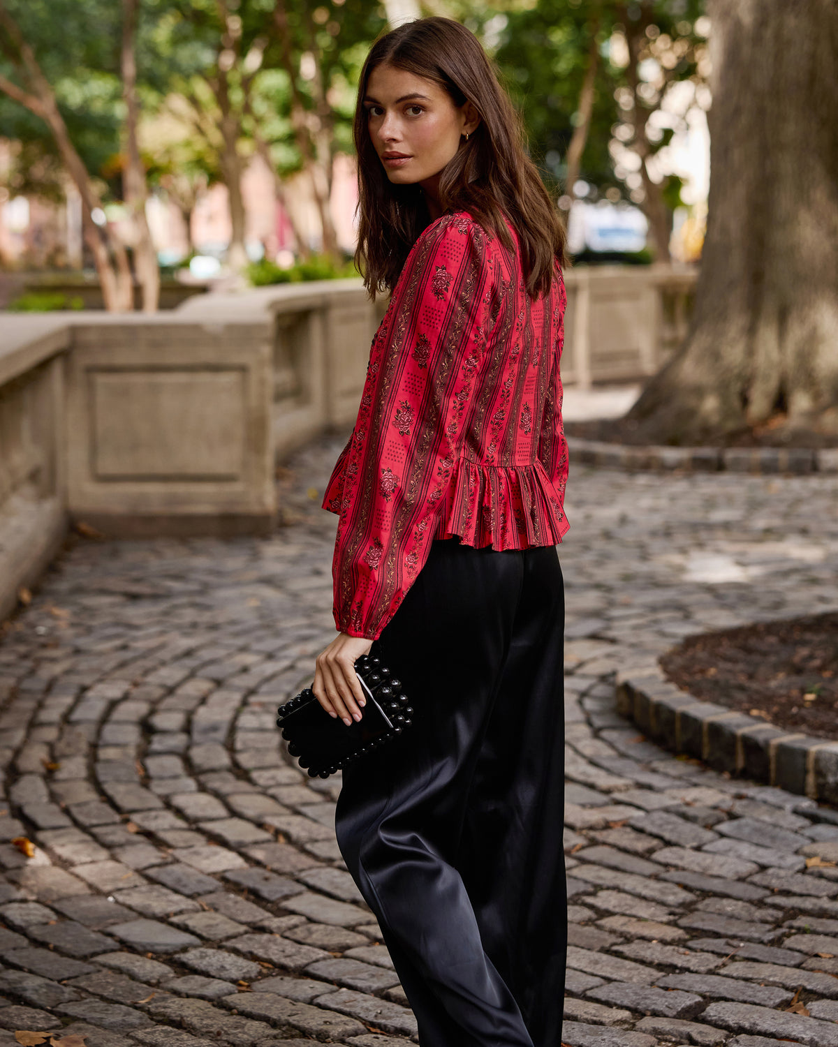 Person wearing the Heirloom Red Festive Roses Lavelle blouse with long sleeves, black pants, and a black clutch.