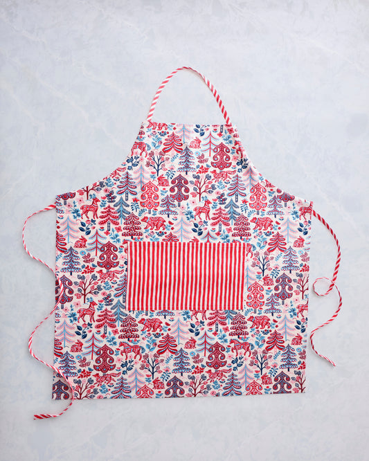 Apron laid flat with a cream background and red, blue, and pink forest-themed print, plus a red-and-white striped center pocket and ties.