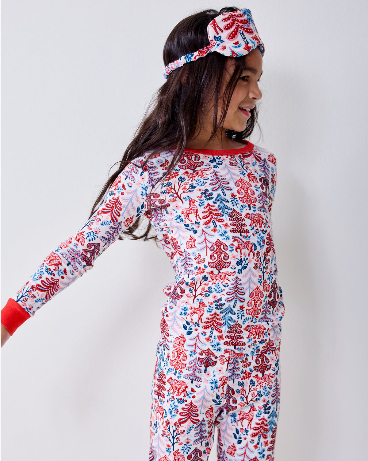 Side view of a child wearing the cream Folklore Forest printed long-sleeve pajama set and matching eye mask.