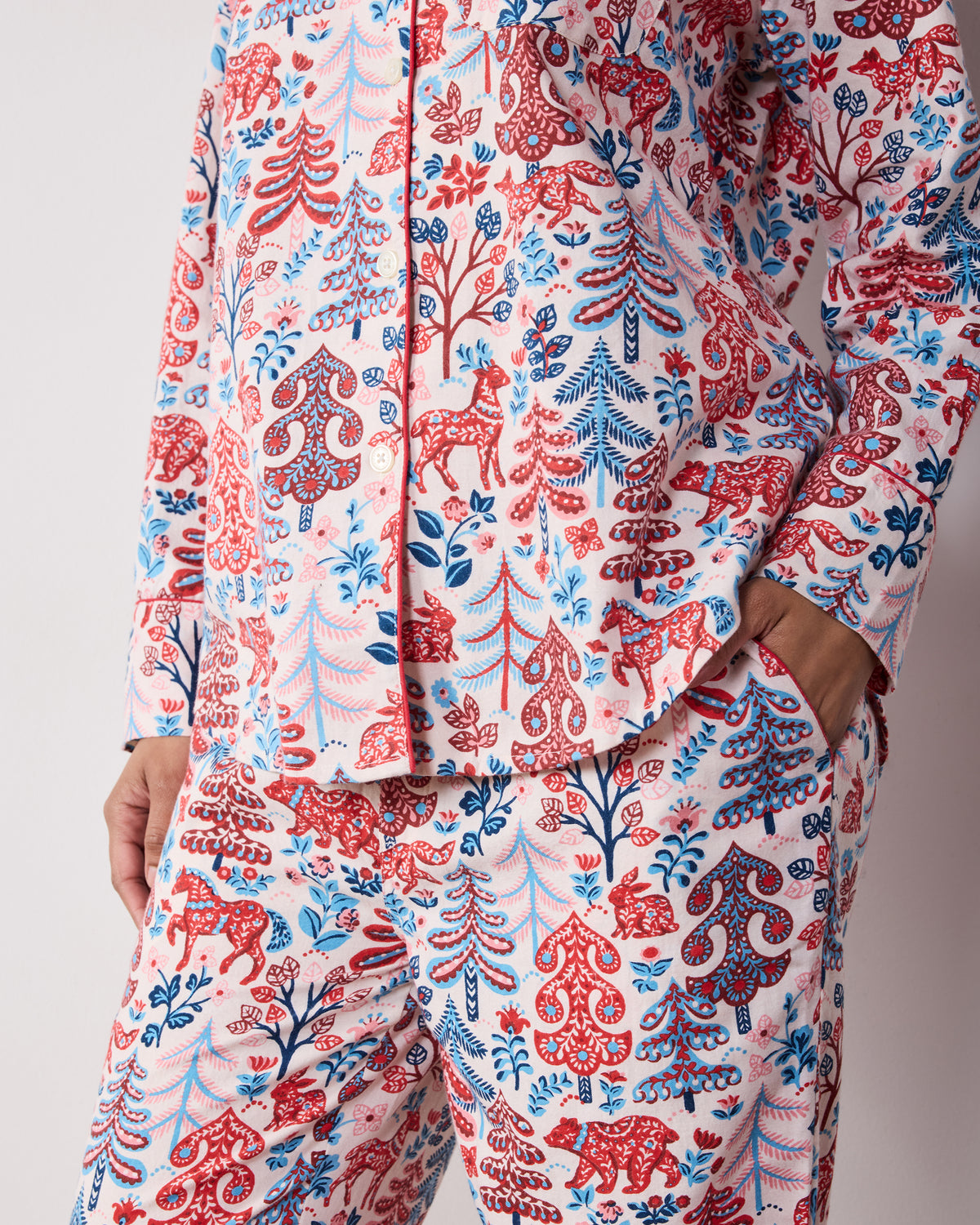 Front detail of the cream Folklore Forest long pajama set with red, blue, and pink forest-inspired print and side pockets.