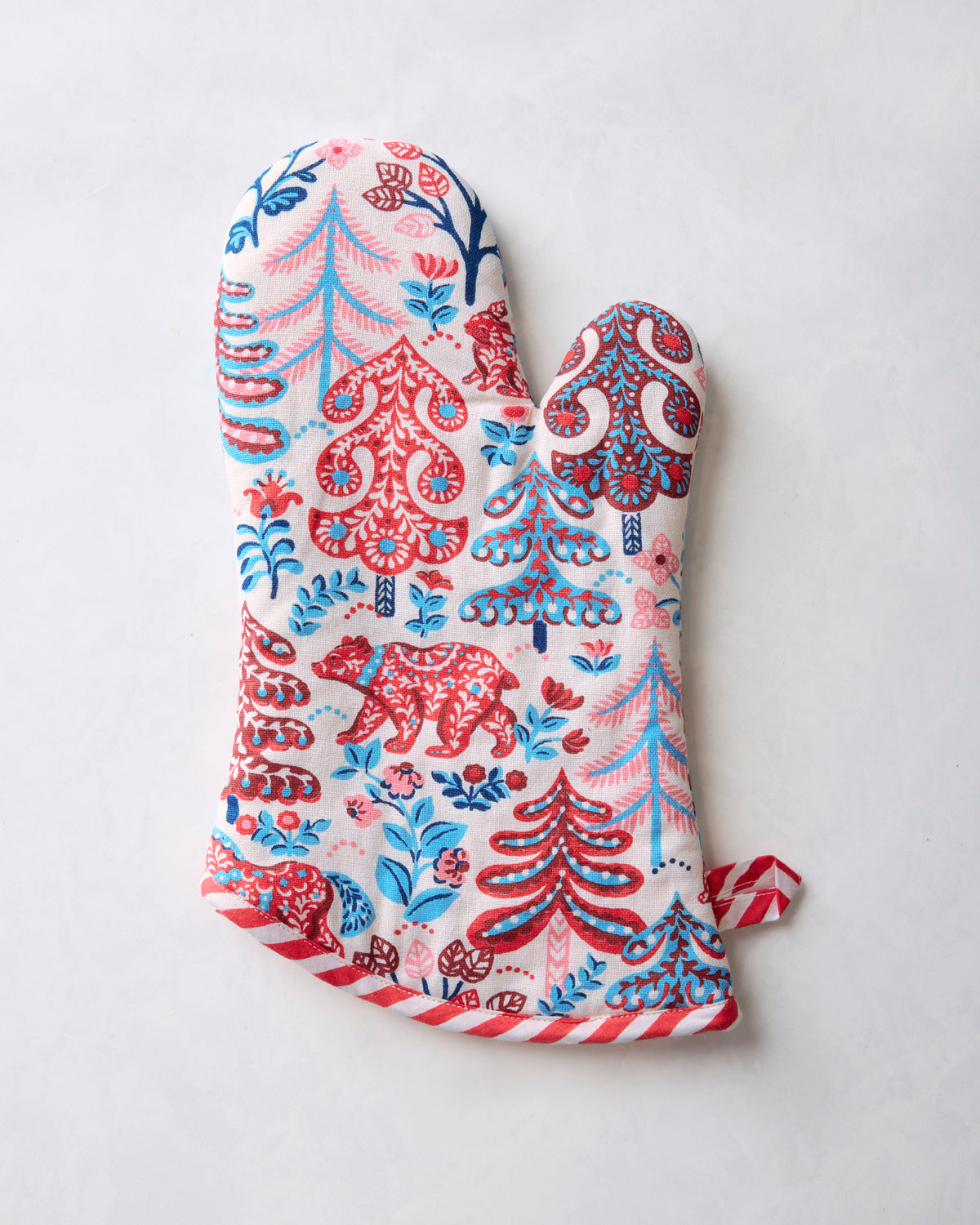 Cream oven mitt with red and blue woodland-pattern print and striped red trim, shown from one side.
