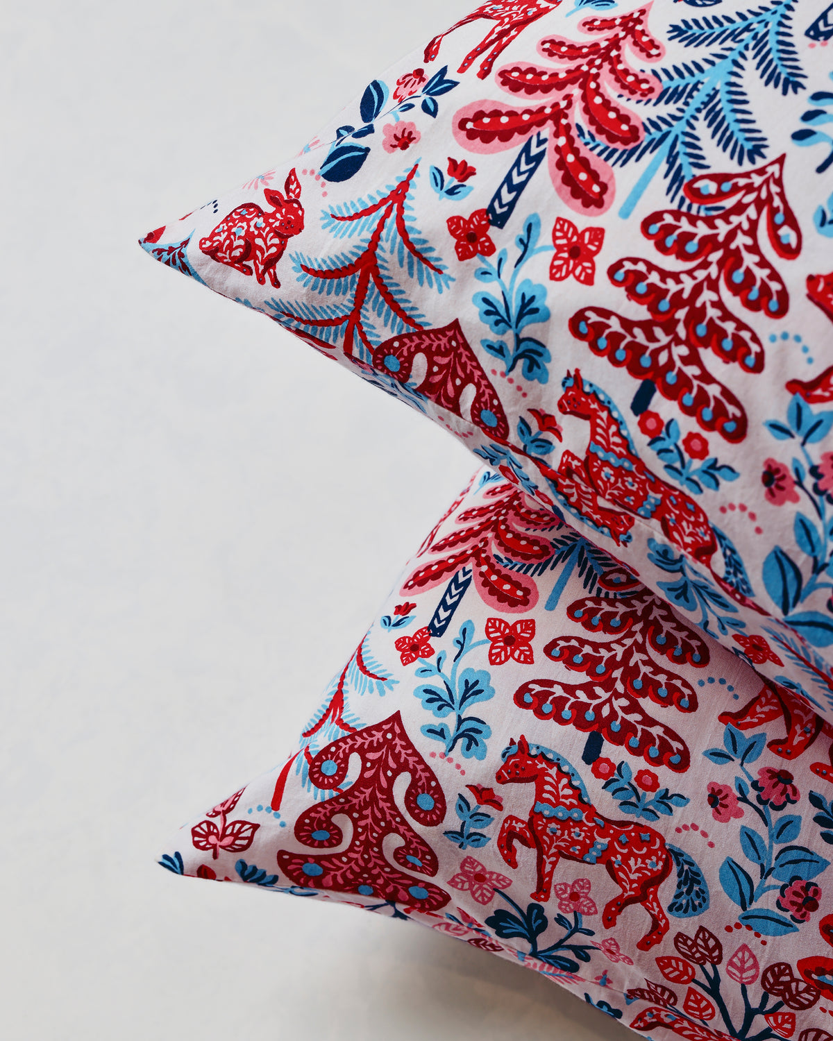 Close-up of overlapping pillowcase corners showing the red, navy, and pink forest print.