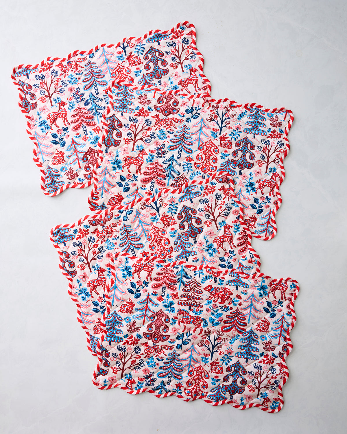 Four Folklore Forest placemats with scalloped edges arranged in an overlapping stack.